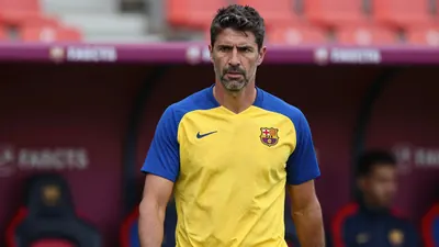 A concerned, mid-30s Barcelona SC coach with a strong build, wearing a plain yellow and blue training top, stands...