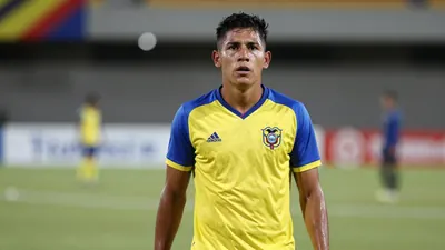 A determined 28-year-old Ecuadorian midfielder, strong build, wearing a plain yellow shirt with blue sleeves, made of...
