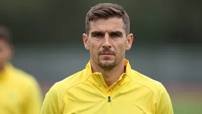 A mid-30s male coach in a solid yellow training jacket, head-and-shoulders framed, background blurred