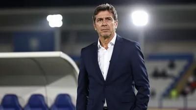 A 45-year-old Argentine coach in a navy blue suit with a white shirt, standing in a stadium tunnel