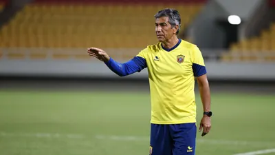 A 35-year-old Ecuadorian assistant coach, with a rugged build and graying temples, stands on the Estadio Rodrigo Paz...