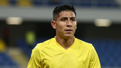 A mid-30s anonymous Ecuadorian player in a solid yellow jersey, head-and-shoulders, focused expression, blurred stadium...