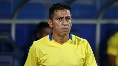A close-up shot of a determined 32-year-old Ecuadorian coach, his weathered face set in a fierce expression, as he stands...